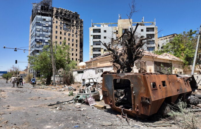 Members of army walks next to destroyed military vehicle and bombed buildings in the state of Khartoum